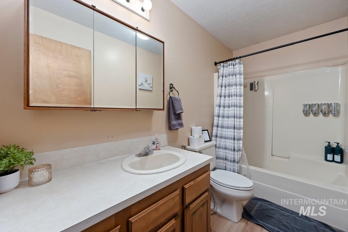 Full bathroom with a textured ceiling, vanity, shower / tub combo, and light wood-style flooring