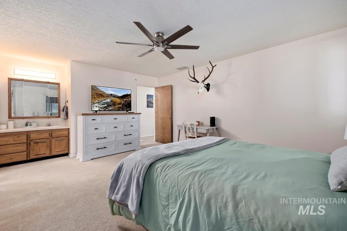 Bedroom with light carpet, ceiling fan, and a textured ceiling