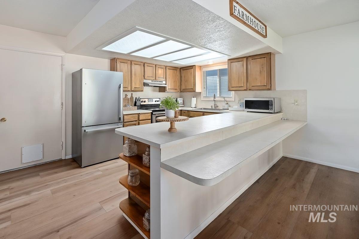 Kitchen with stainless steel appliances, light countertops, a peninsula, light wood-style flooring, and open shelves
