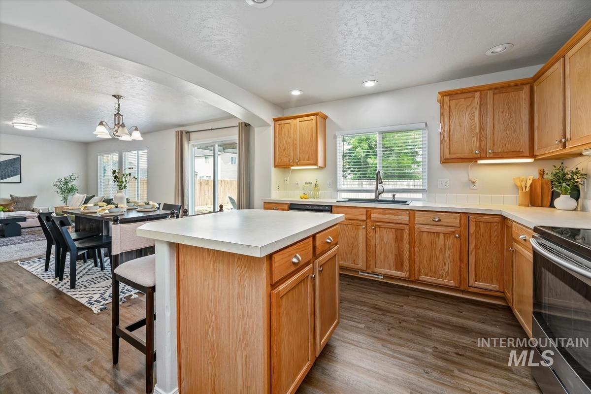 Kitchen featuring a kitchen island, a kitchen breakfast bar, a textured ceiling, light countertops, and dark wood-style flooring