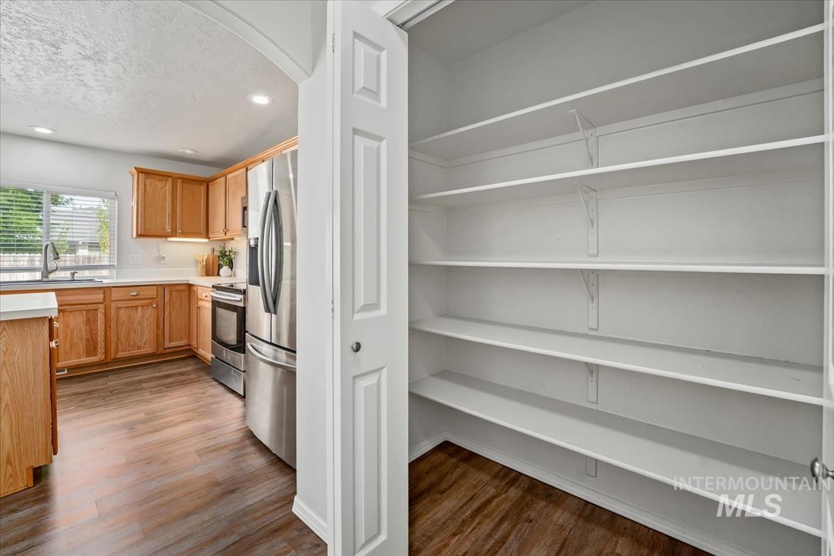 Kitchen with light countertops, appliances with stainless steel finishes, dark wood finished floors, a textured ceiling, and recessed lighting