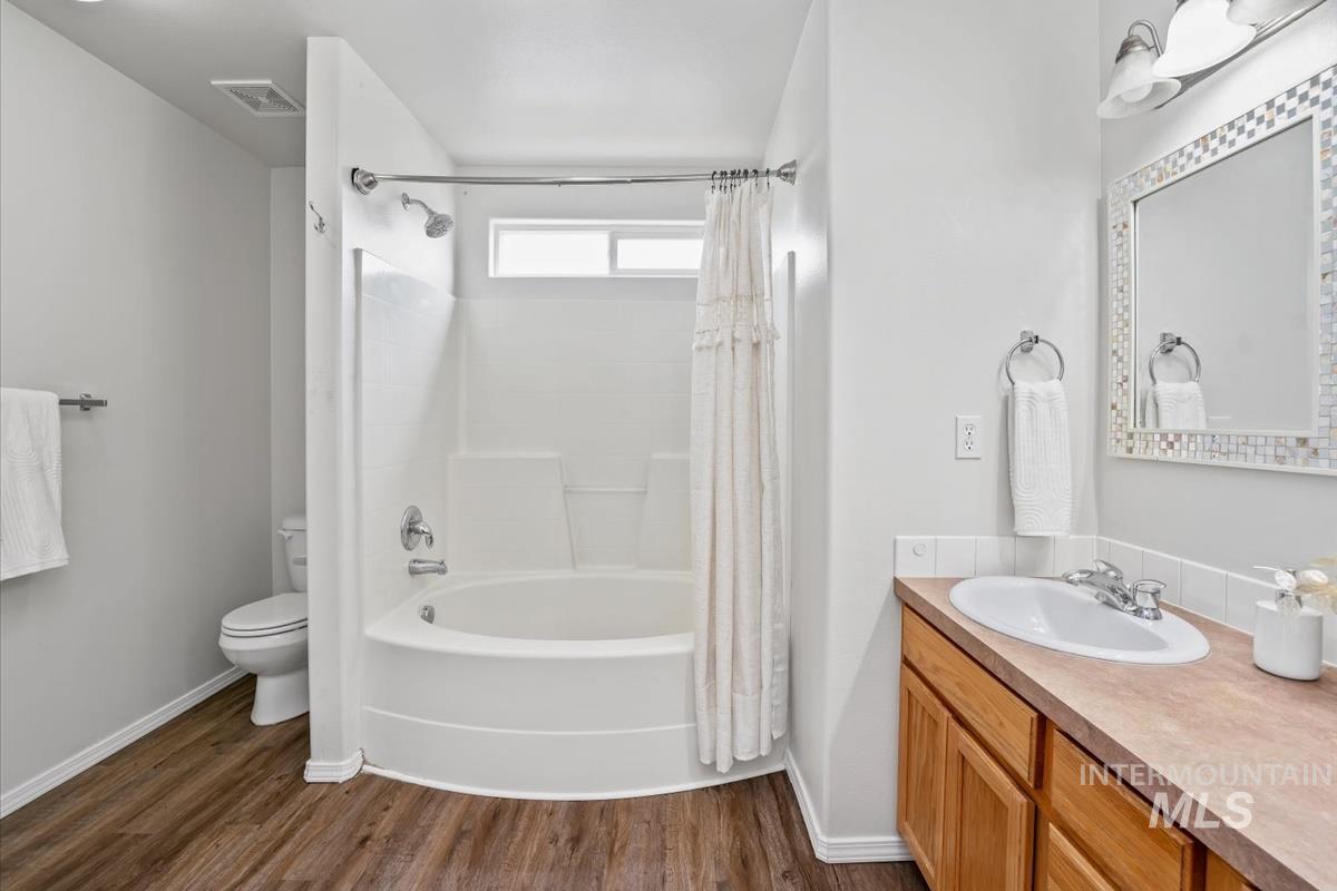 Full bath featuring shower / bathtub combination with curtain, vanity, and dark wood-style floors