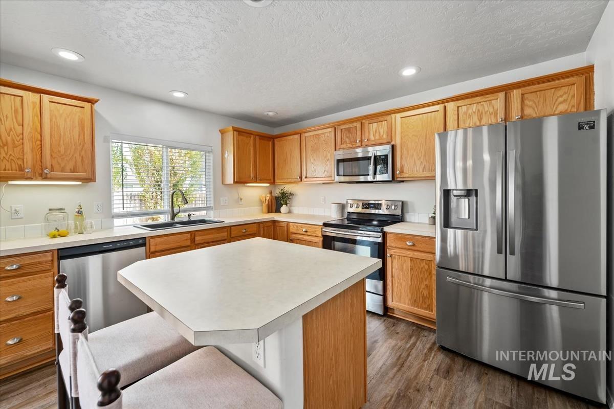 Kitchen featuring stainless steel appliances, recessed lighting, light countertops, a center island, and dark wood-style floors