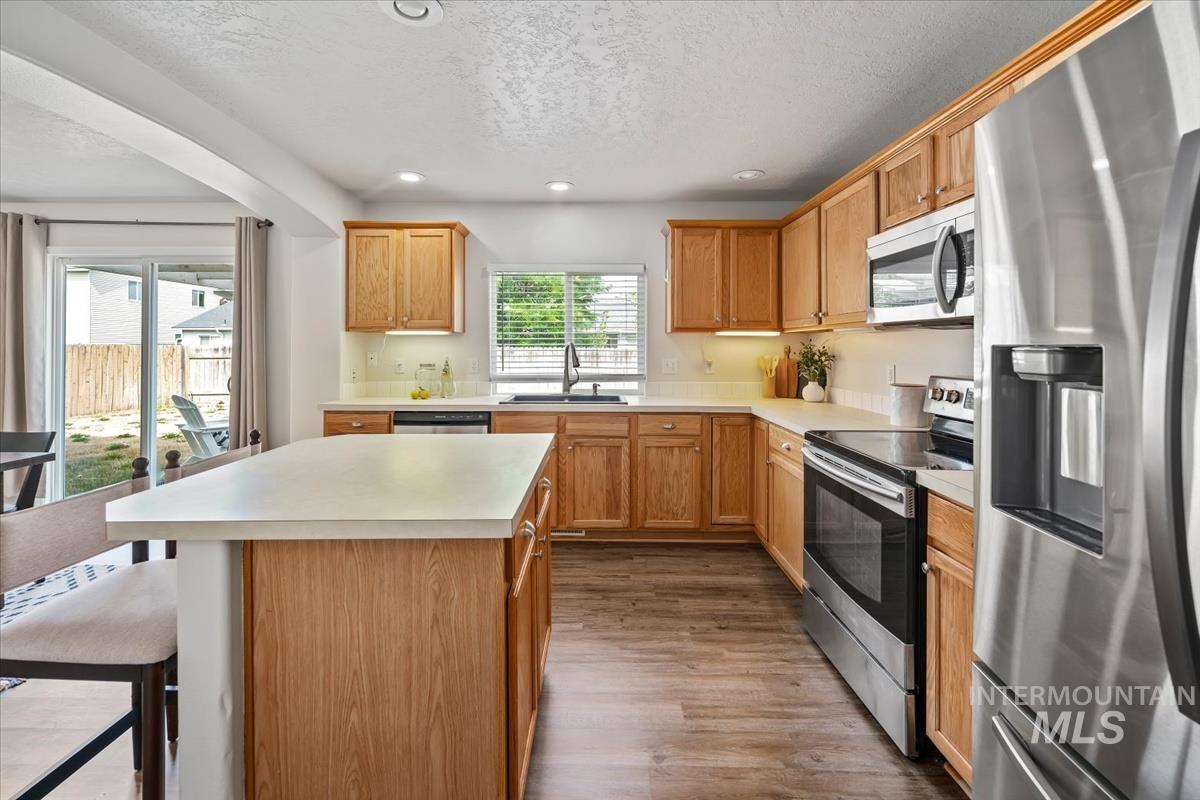 Kitchen featuring stainless steel appliances, light countertops, a kitchen island, recessed lighting, and a textured ceiling