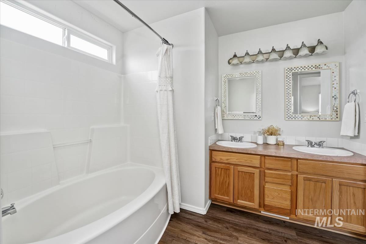 Full bathroom featuring shower / tub combo with curtain, double vanity, and dark wood-style flooring