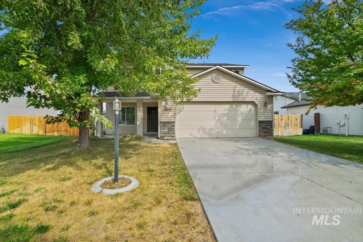 View of property hidden behind natural elements with driveway, stone siding, and an attached garage