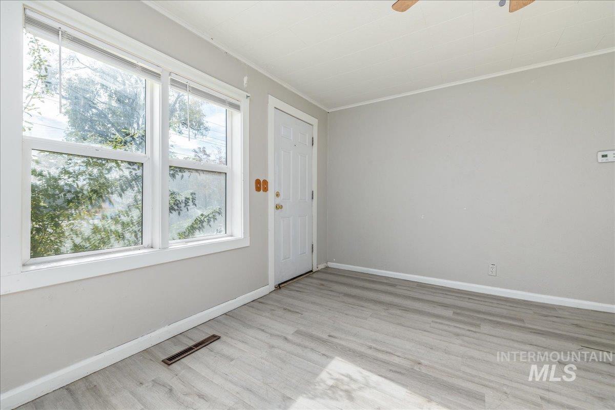 Empty room with light wood-type flooring, ornamental molding, and ceiling fan