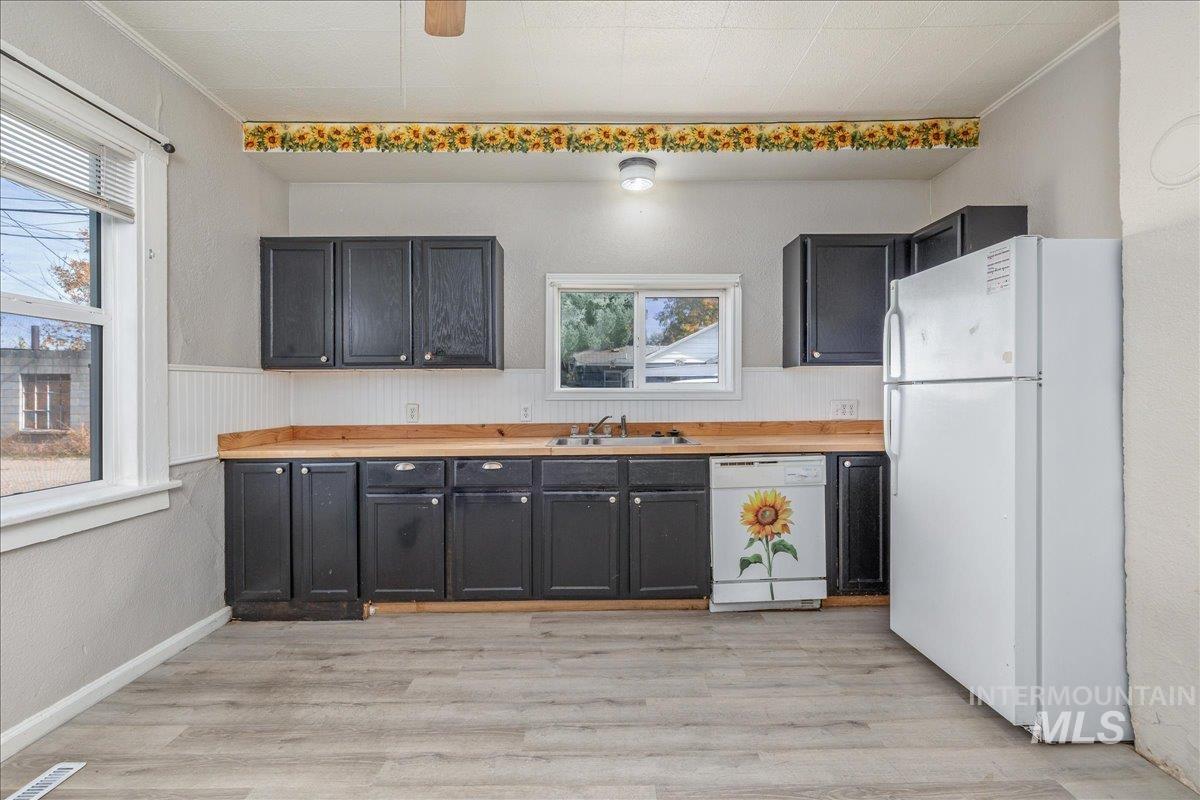 Kitchen with white appliances, dark cabinetry, light wood-style floors, a textured wall, and a wainscoted wall