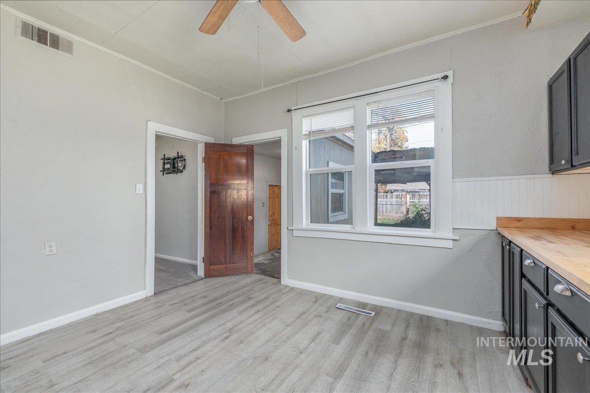 Unfurnished dining area with light wood-style floors, a ceiling fan, ornamental molding, and wainscoting
