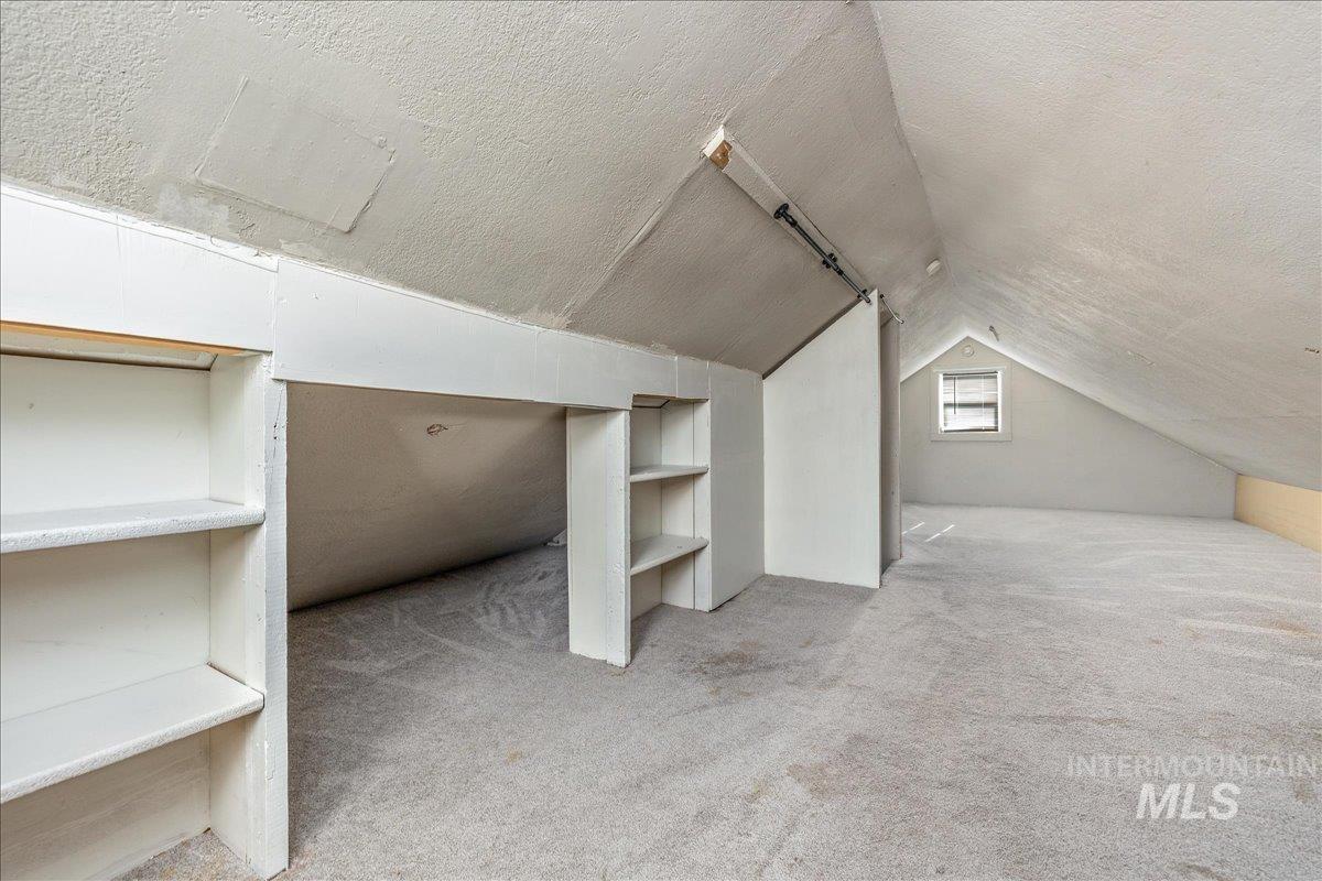 Additional living space with a textured ceiling, carpet flooring, lofted ceiling, and built in features