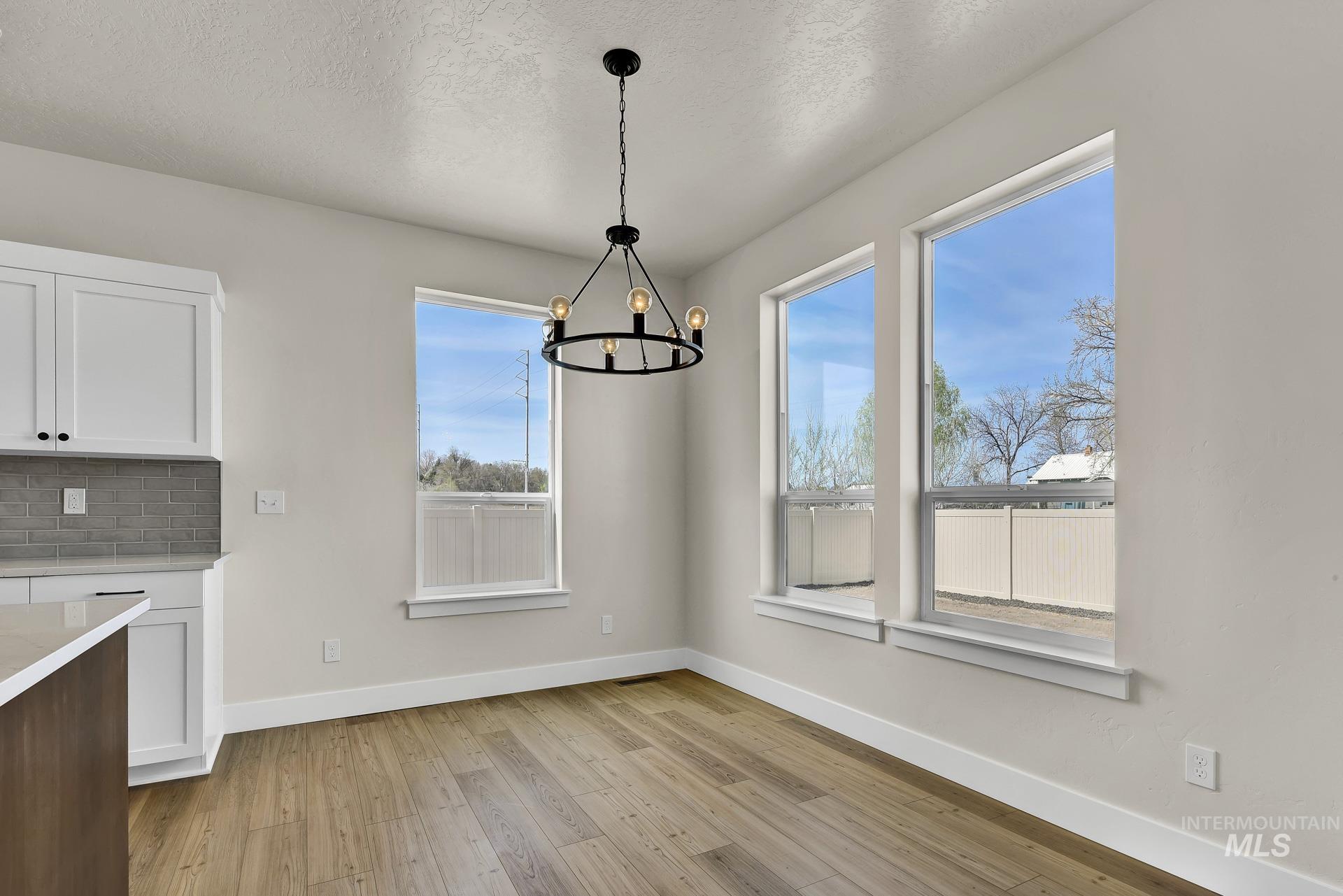 Unfurnished dining area with light wood-style flooring, a chandelier, and a textured ceiling