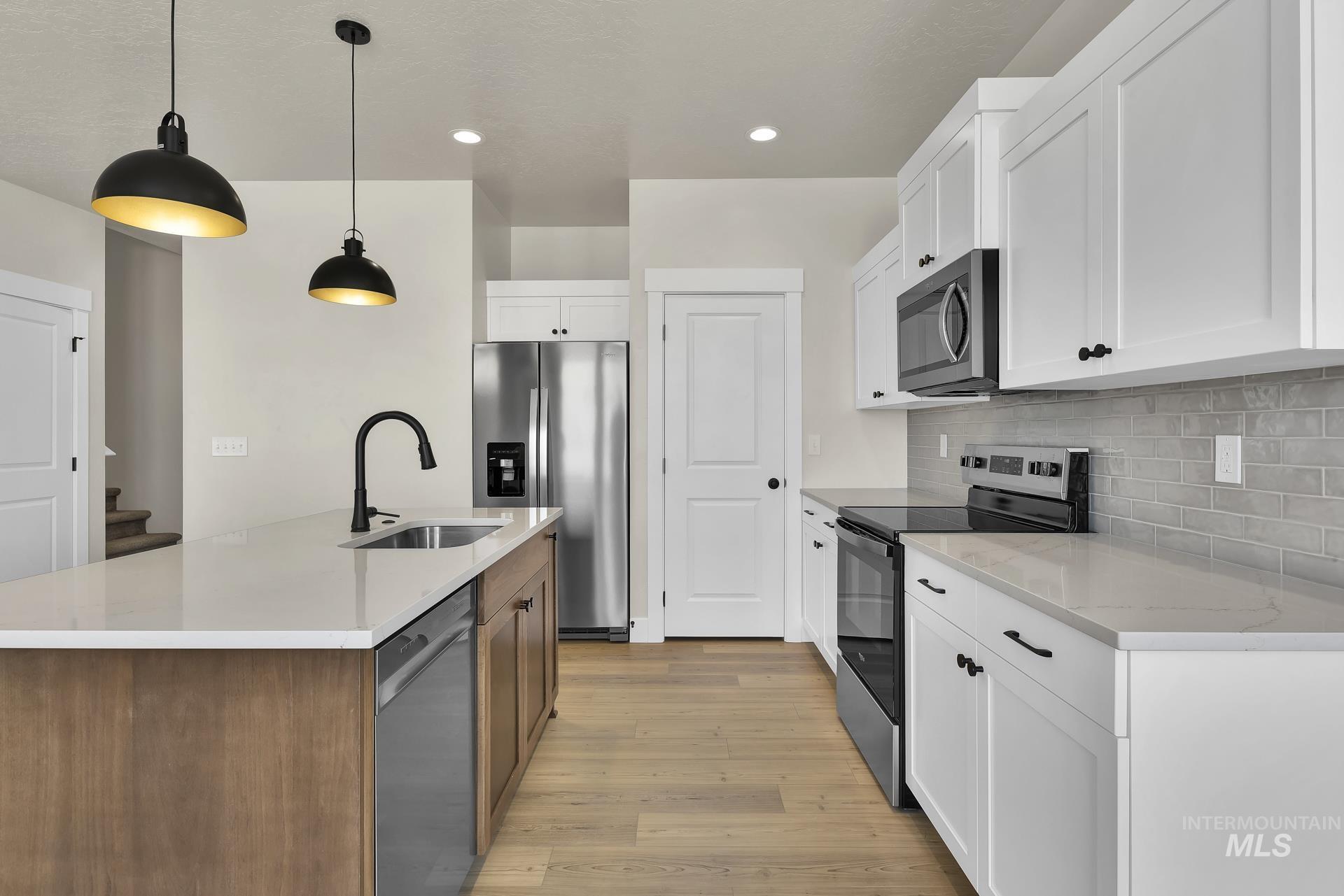 Kitchen featuring stainless steel appliances, a kitchen island with sink, hanging light fixtures, white cabinetry, and light wood-style flooring