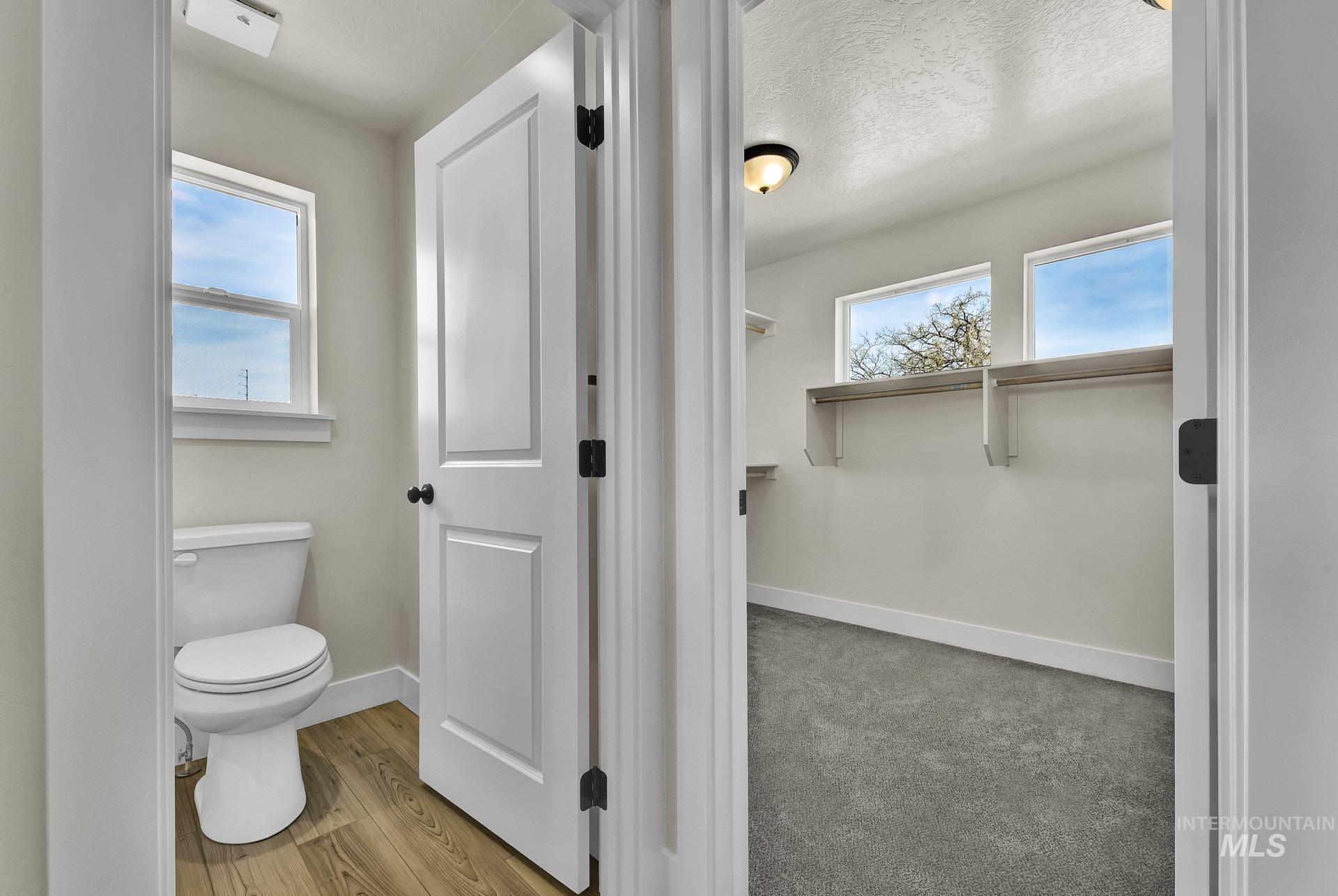 Bathroom with healthy amount of natural light, light wood-type flooring, a textured ceiling, and a walk in closet