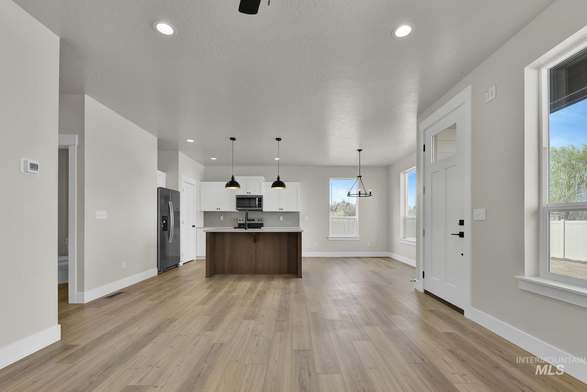 Kitchen with light countertops, pendant lighting, an island with sink, white cabinetry, and open floor plan
