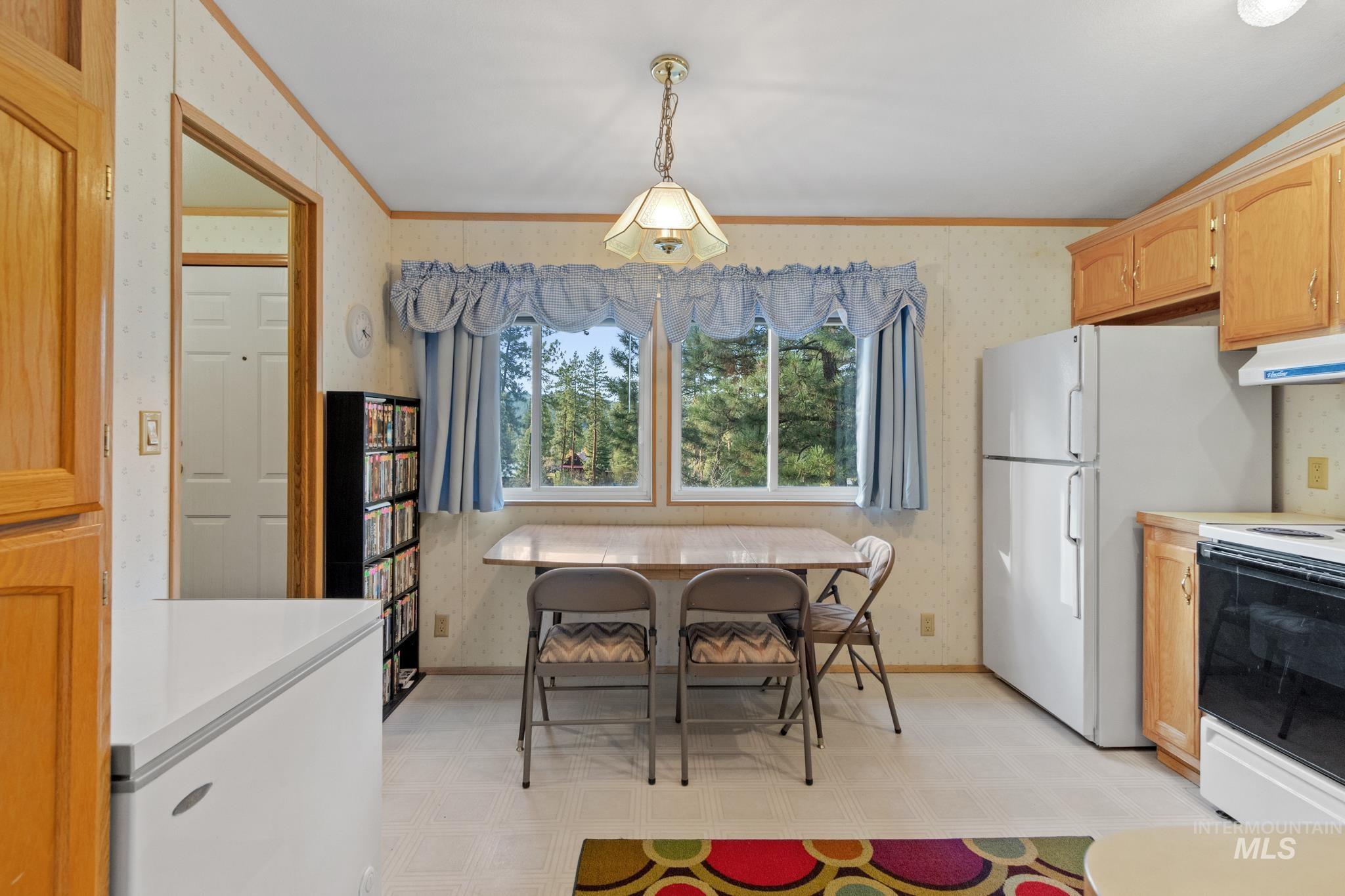 Kitchen featuring wallpapered walls, light countertops, white electric range oven, hanging light fixtures, and ornamental molding