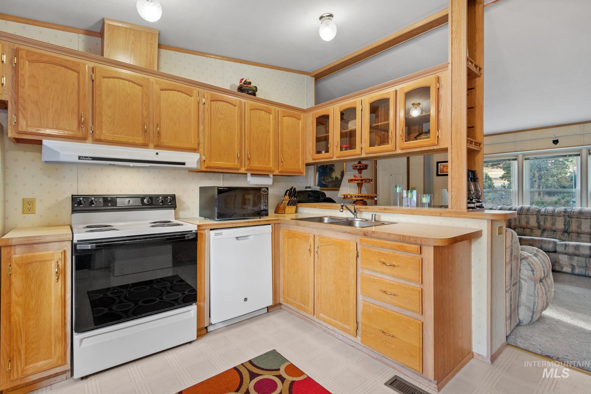 Kitchen with white appliances, wallpapered walls, glass insert cabinets, light countertops, and light flooring