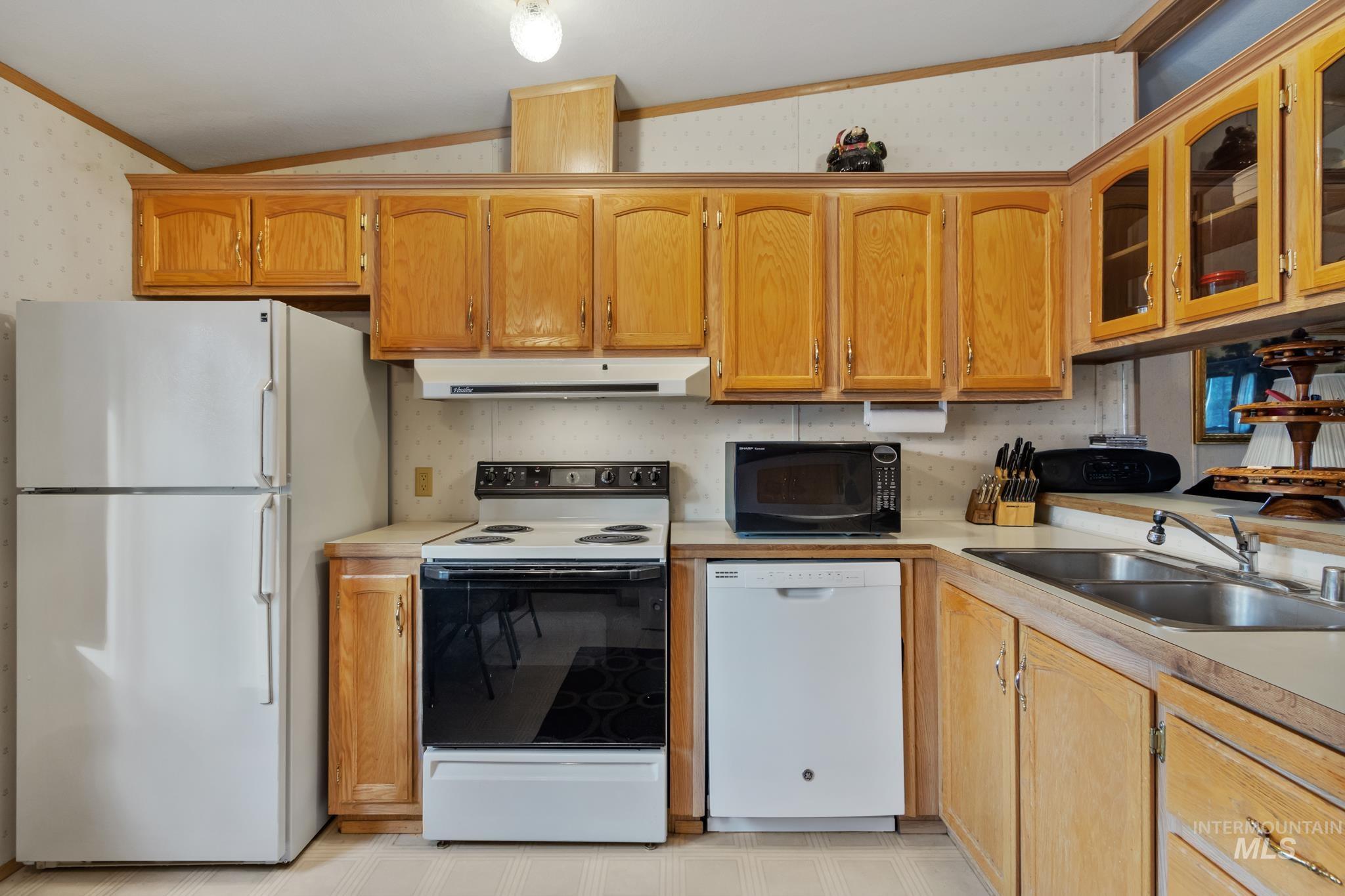 Kitchen with white appliances, wallpapered walls, light countertops, lofted ceiling, and glass insert cabinets