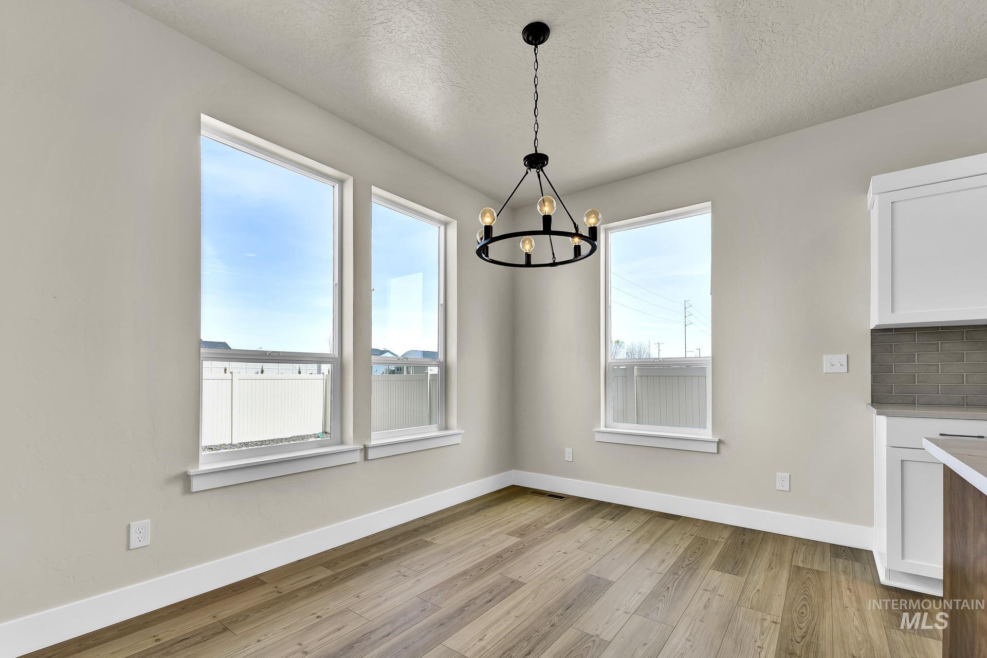 Unfurnished dining area with light wood-type flooring, a textured ceiling, and a chandelier