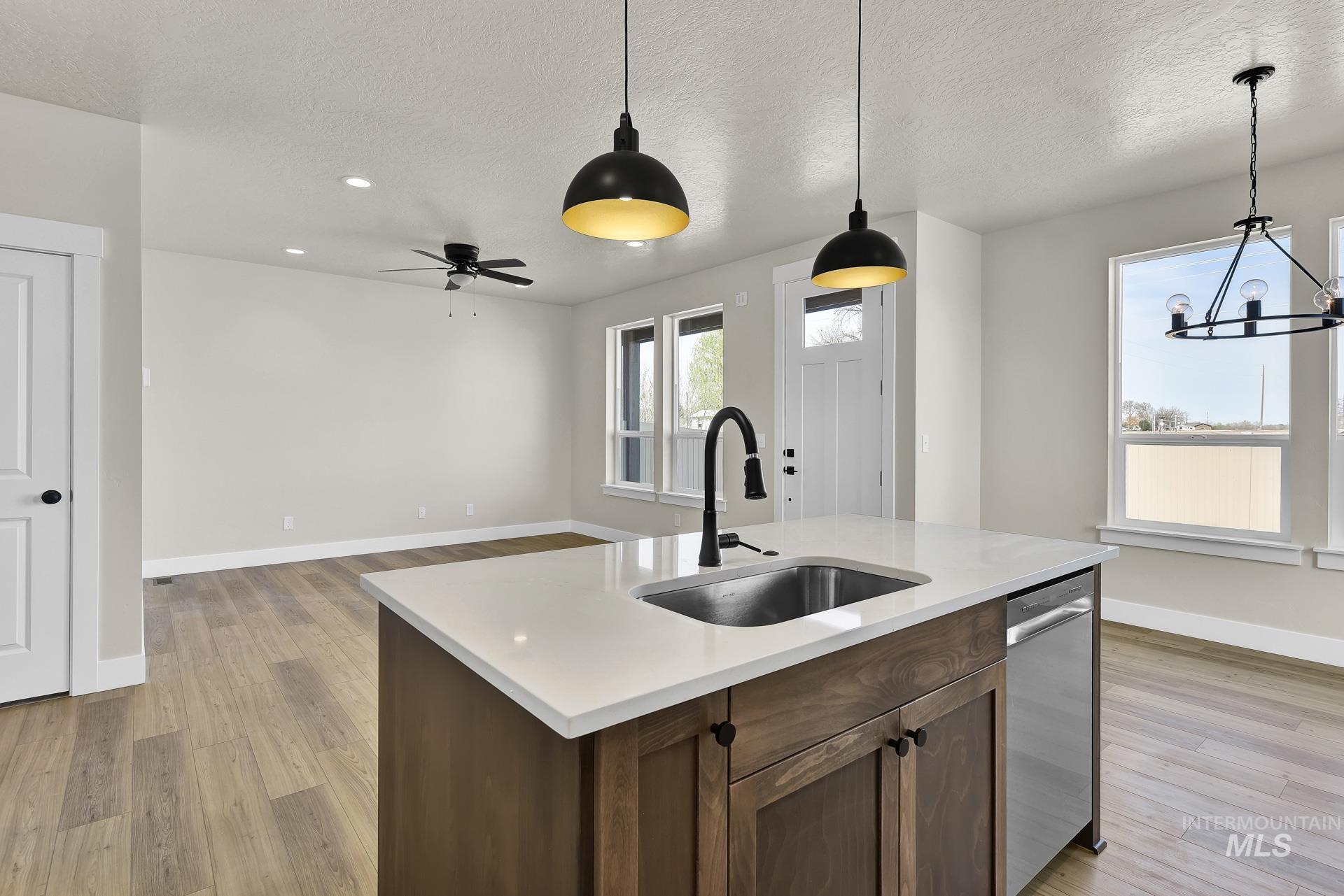 Kitchen featuring decorative light fixtures, light wood-style flooring, stainless steel dishwasher, a textured ceiling, and an island with sink
