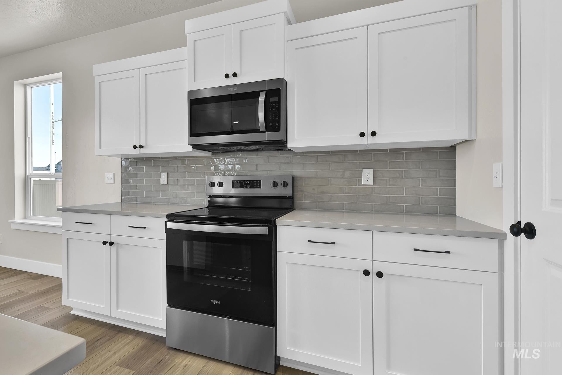 Kitchen featuring stainless steel appliances, white cabinetry, backsplash, light wood finished floors, and a textured ceiling