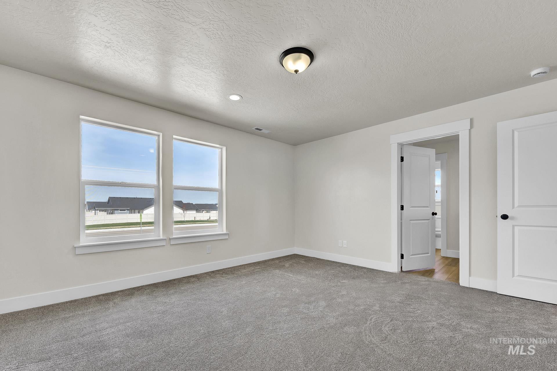 Carpeted spare room with a textured ceiling and baseboards