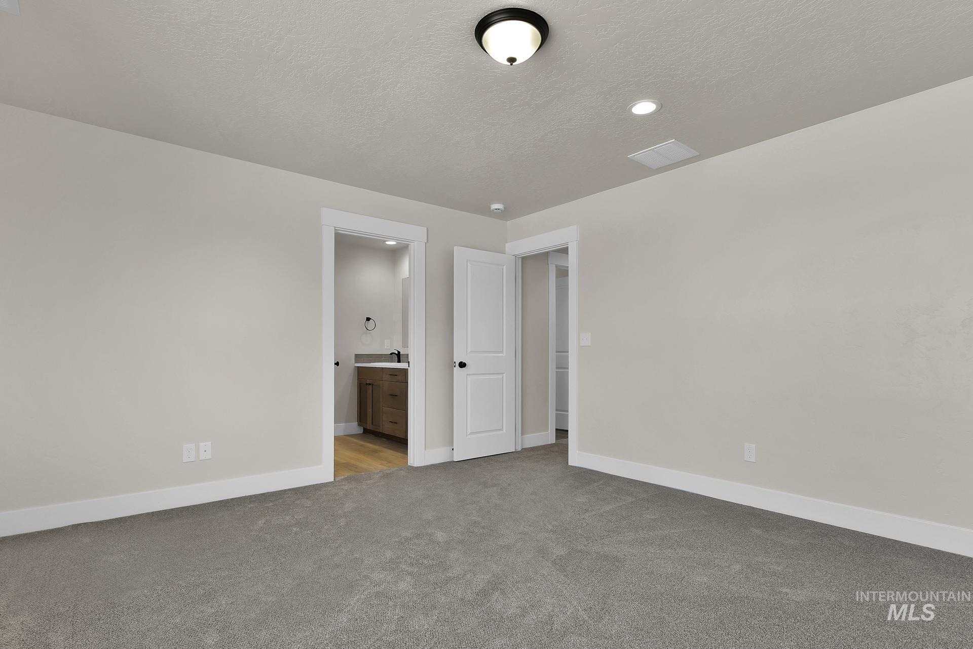 Unfurnished bedroom with a textured ceiling, light carpet, and connected bathroom