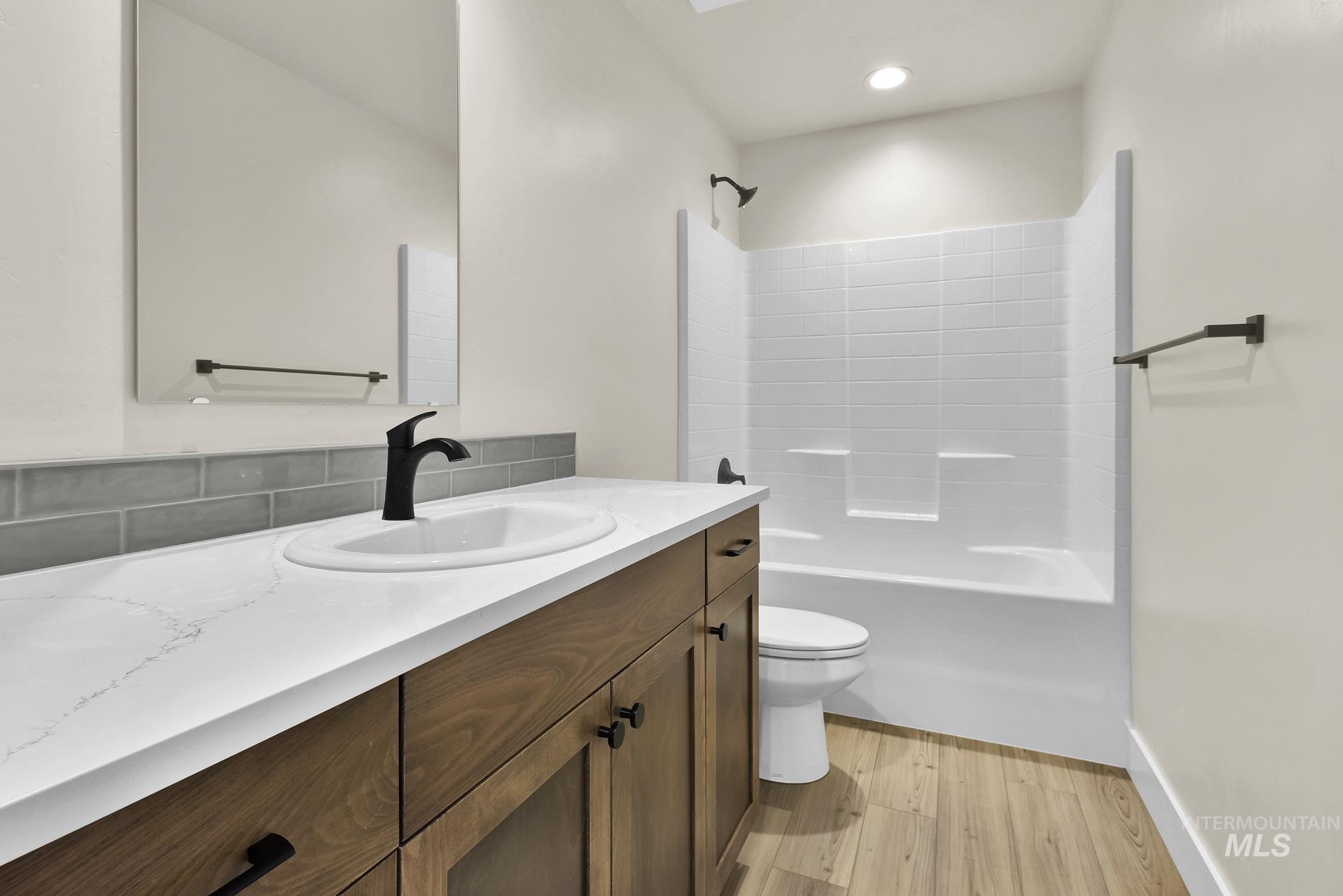 Bathroom featuring light wood-style flooring, vanity, shower / tub combination, backsplash, and recessed lighting