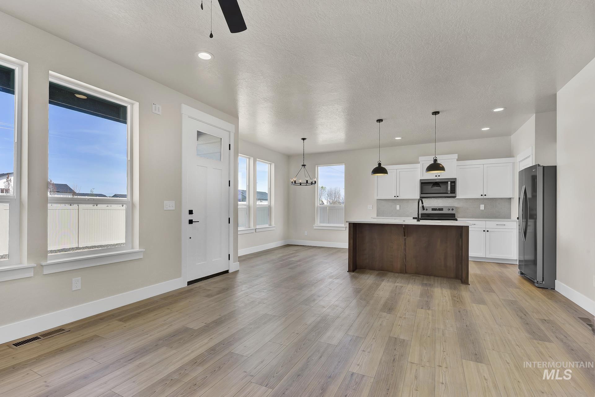 Kitchen with stainless steel appliances, white cabinetry, a kitchen island with sink, open floor plan, and backsplash