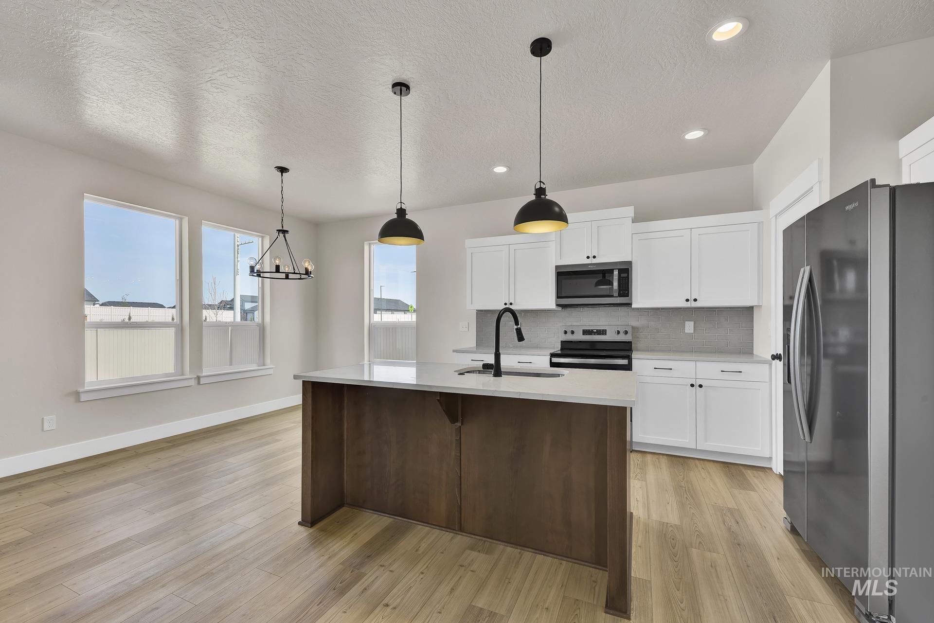 Kitchen featuring appliances with stainless steel finishes, white cabinetry, a textured ceiling, decorative light fixtures, and decorative backsplash