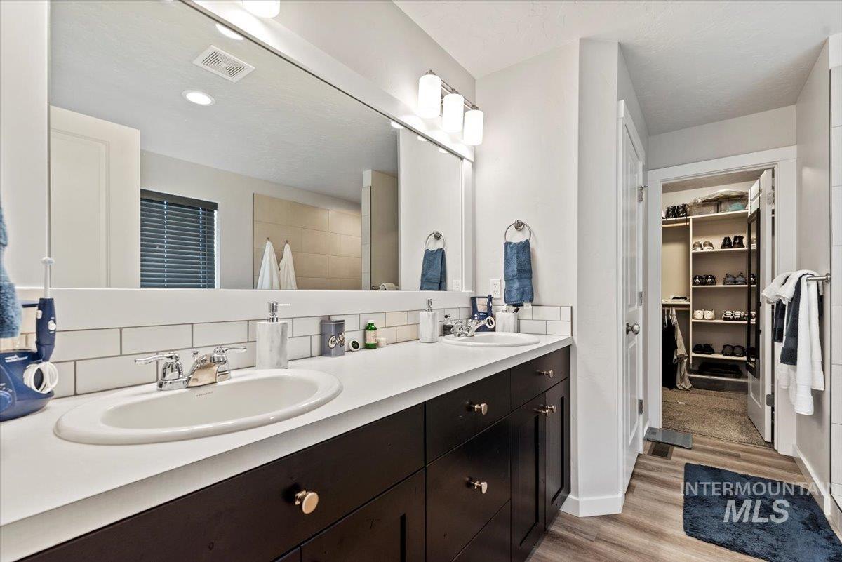 Bathroom featuring double vanity, a spacious closet, backsplash, and wood finished floors