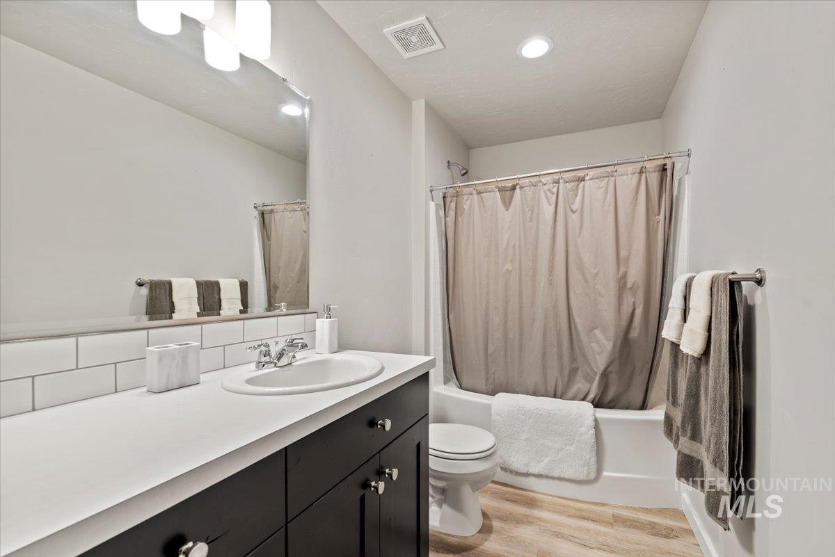 Bathroom featuring vanity, wood finished floors, shower / bathtub combination with curtain, and recessed lighting