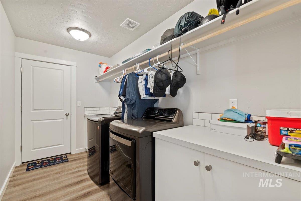 Laundry room with separate washer and dryer, light wood finished floors, and a textured ceiling