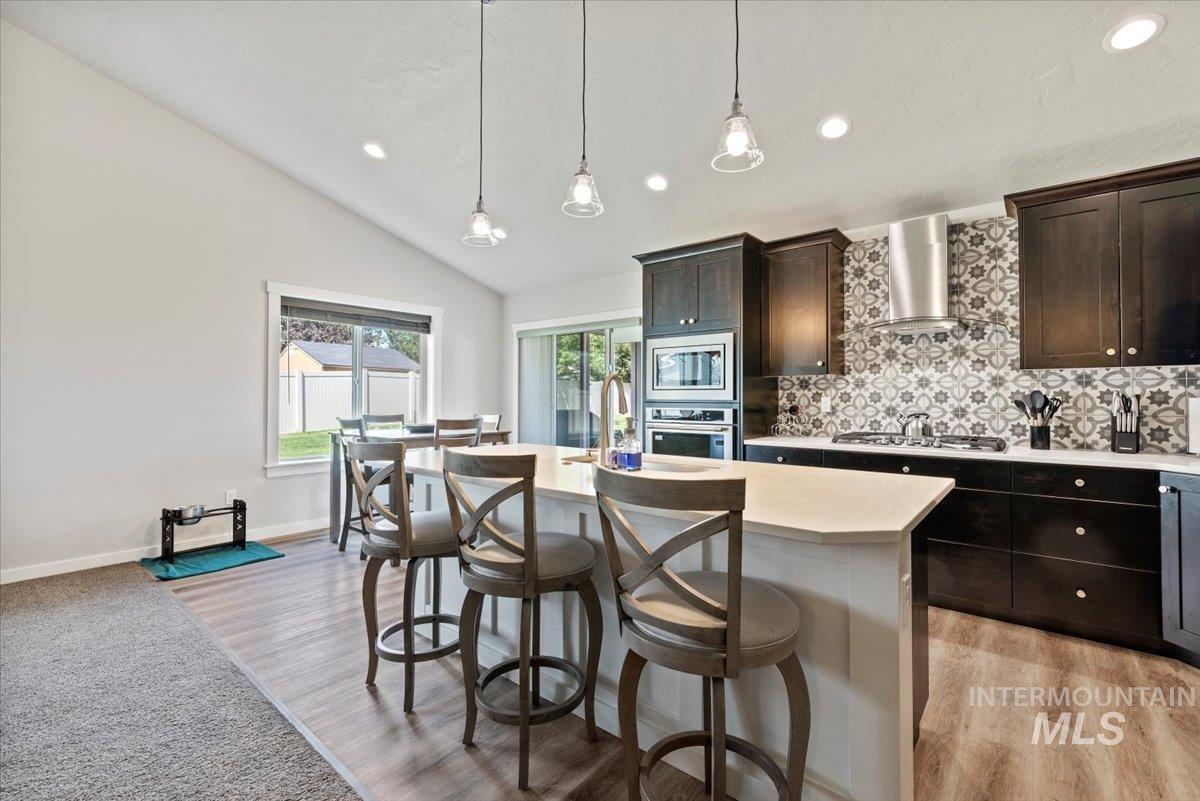 Kitchen featuring backsplash, light countertops, a breakfast bar area, an island with sink, and vaulted ceiling