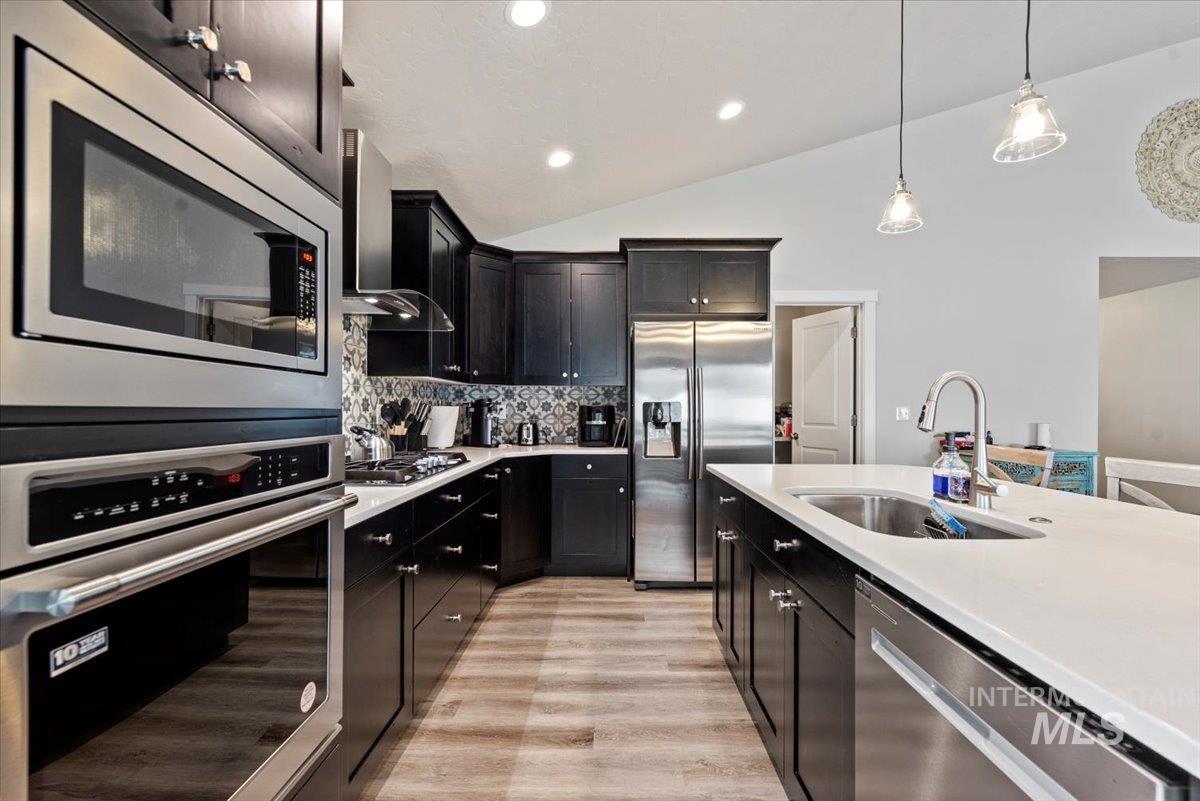 Kitchen featuring appliances with stainless steel finishes, wall chimney range hood, light countertops, tasteful backsplash, and lofted ceiling