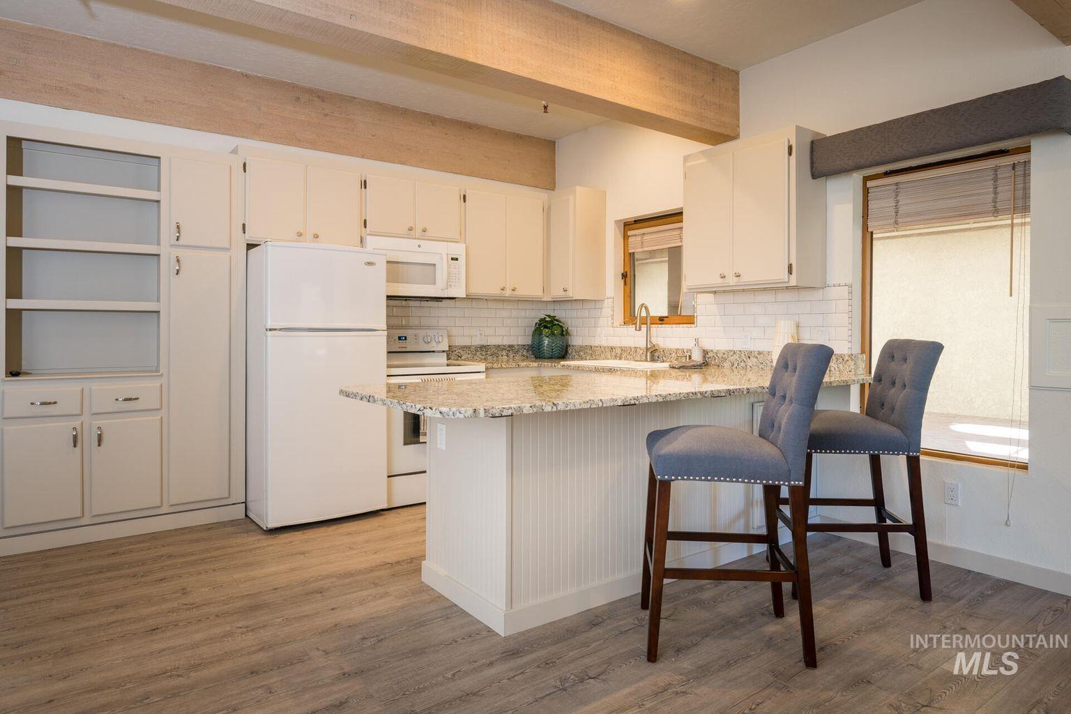 Kitchen featuring white appliances, tasteful backsplash, light wood-style flooring, white cabinetry, and beam ceiling