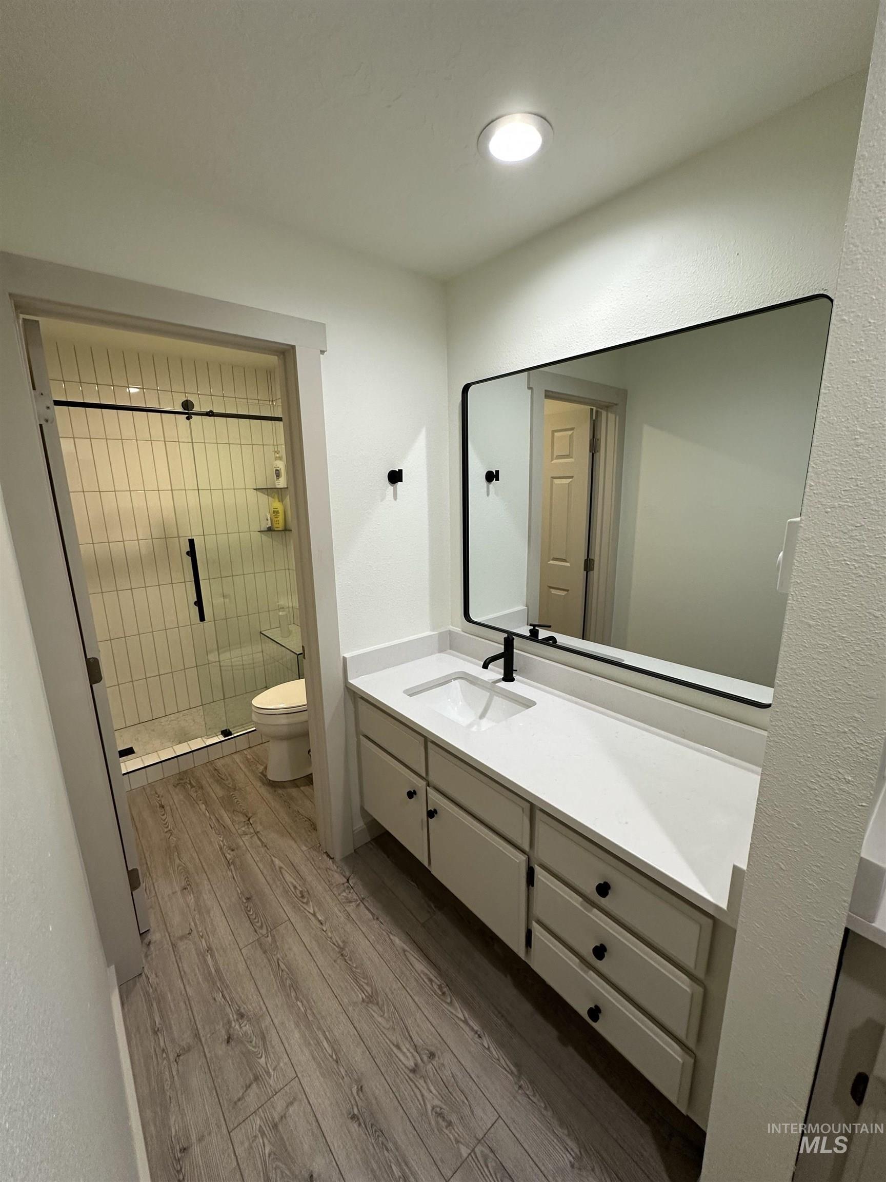 Full bath with vanity, a stall shower, light wood-style floors, and a textured wall