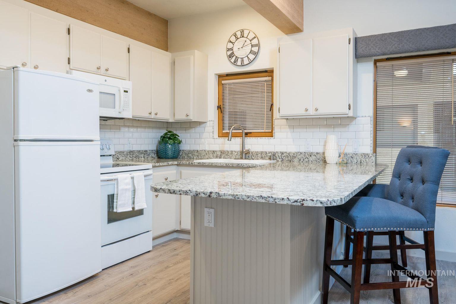 Kitchen featuring white appliances, light wood-style flooring, white cabinets, a peninsula, and decorative backsplash
