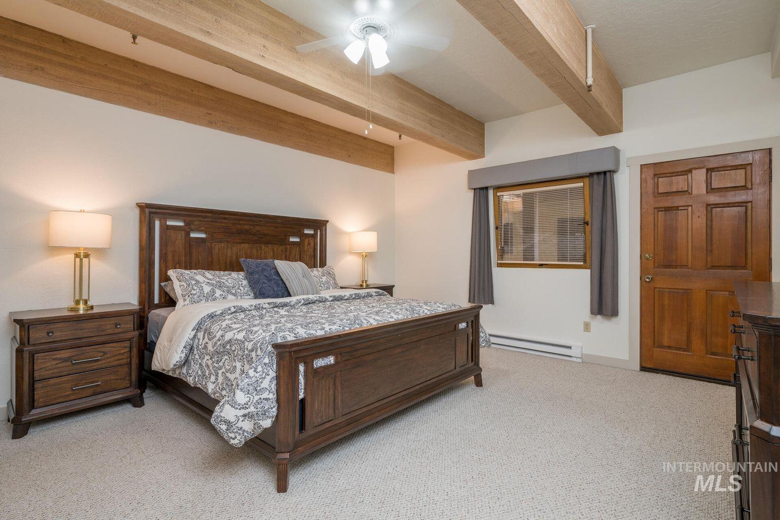 Bedroom with beamed ceiling, light carpet, baseboard heating, and a ceiling fan