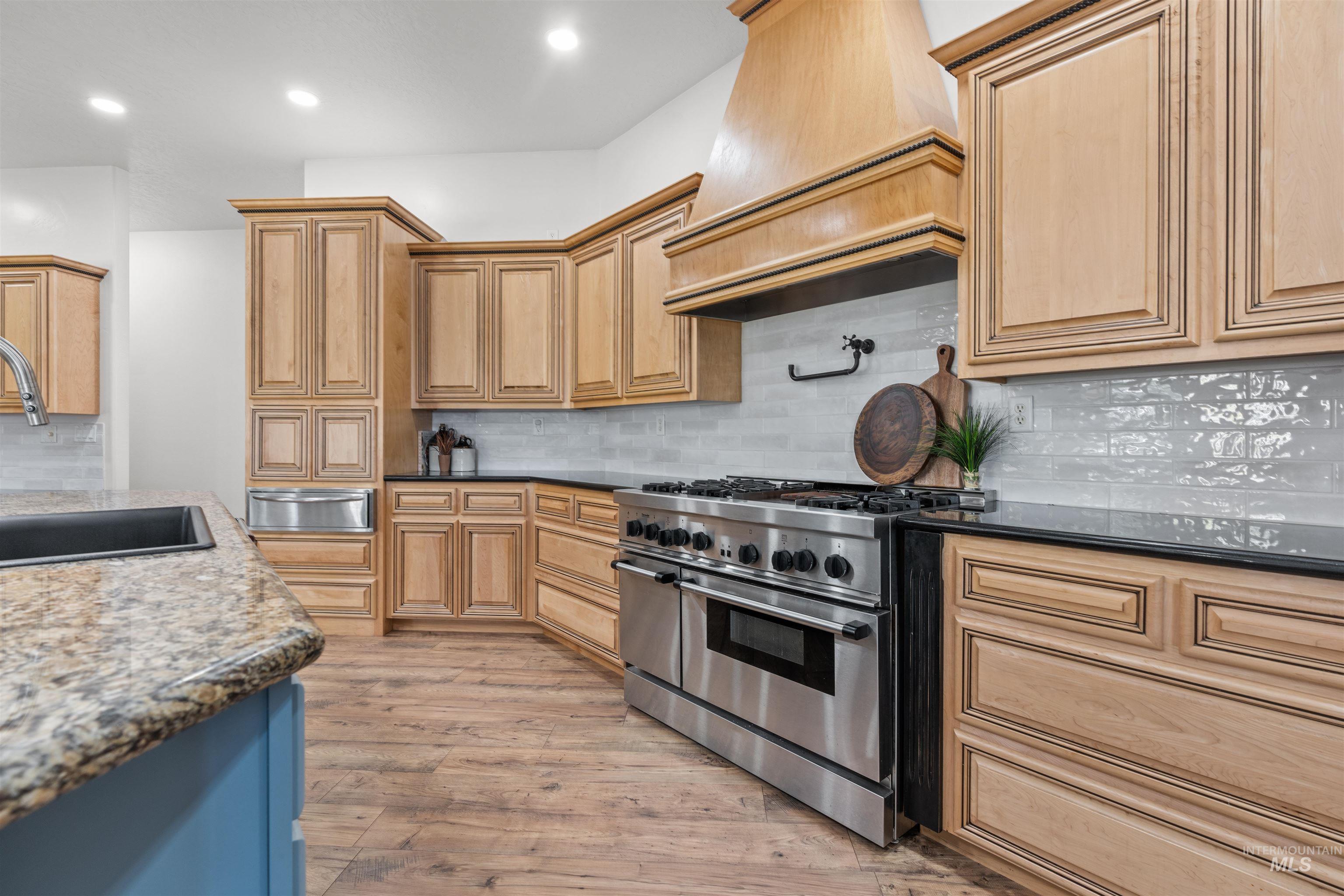Kitchen with backsplash, dark stone countertops, range with two ovens, light wood finished floors, and recessed lighting