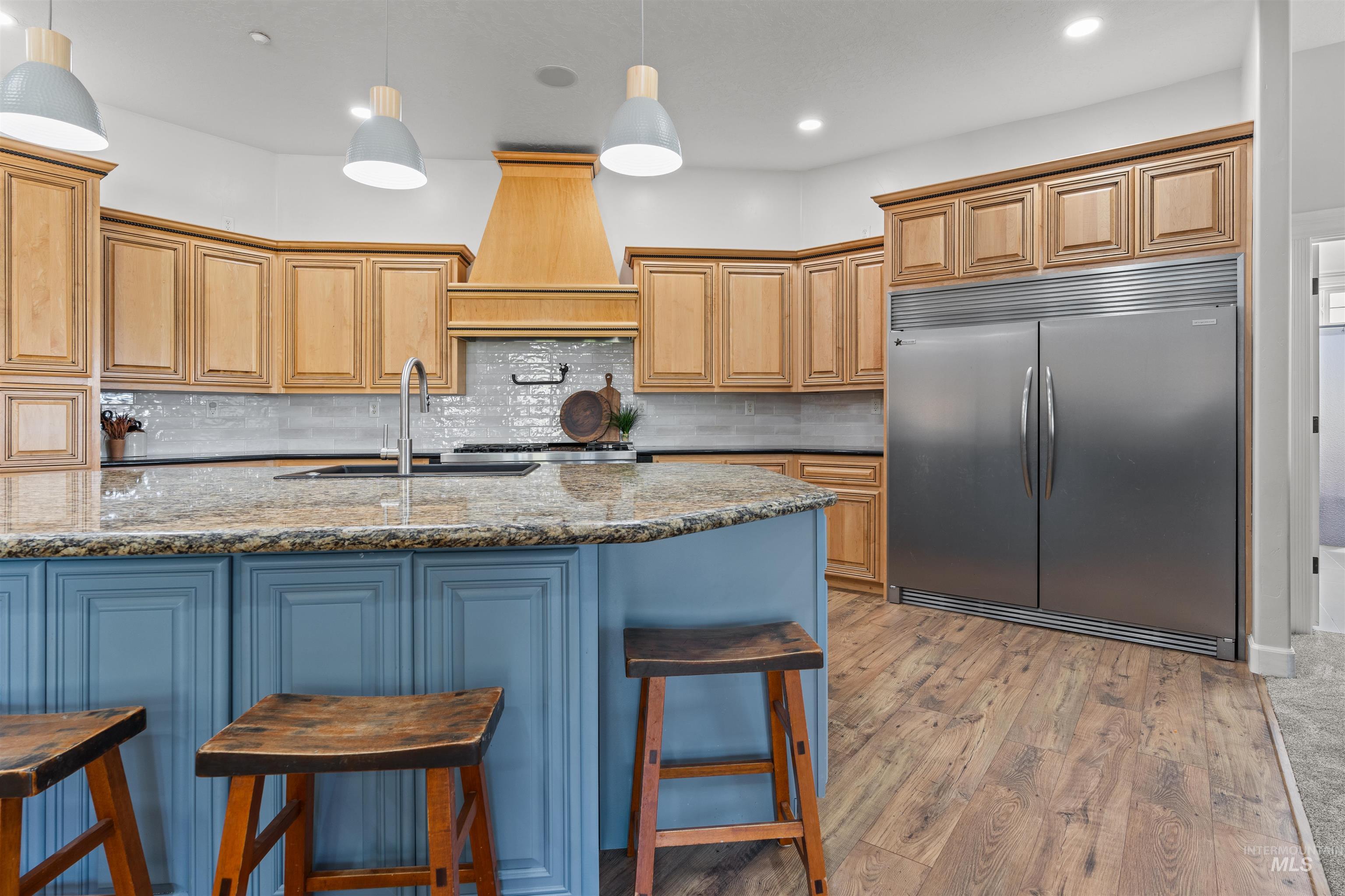 Kitchen featuring a kitchen bar, stainless steel built in refrigerator, tasteful backsplash, dark stone counters, and light wood-style floors