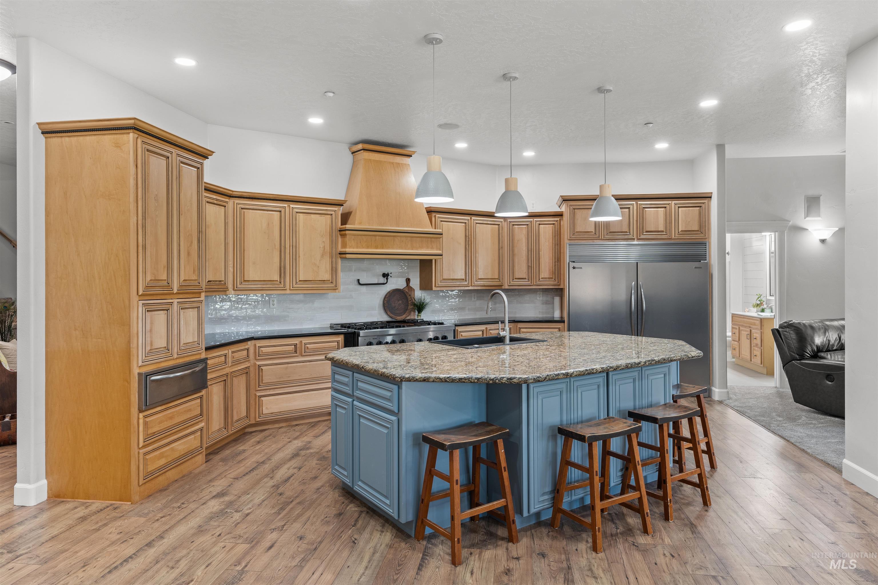 Kitchen with hanging light fixtures, decorative backsplash, a breakfast bar area, light wood finished floors, and a kitchen island with sink