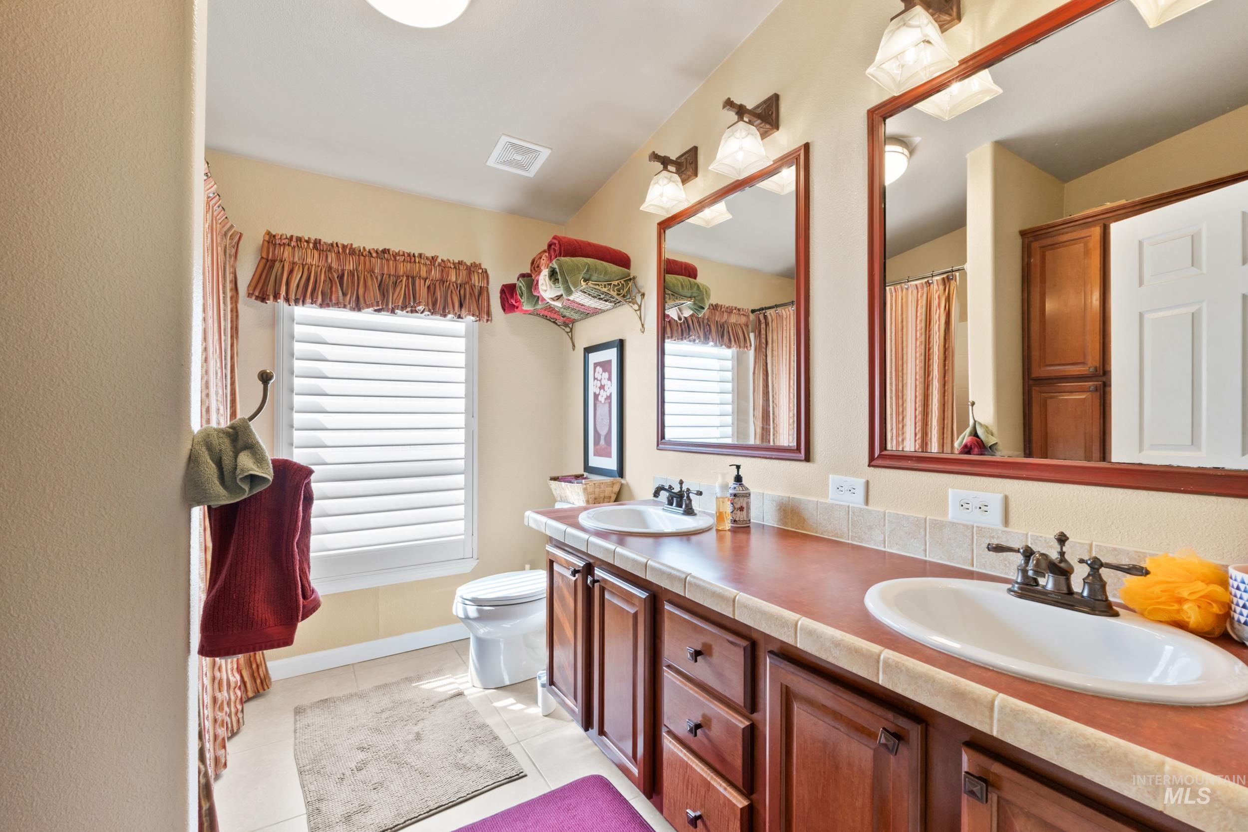 Full bath with double vanity, light tile patterned floors, and a shower with curtain