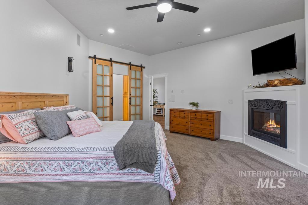 Carpeted bedroom with a barn door, a glass covered fireplace, ceiling fan, and recessed lighting