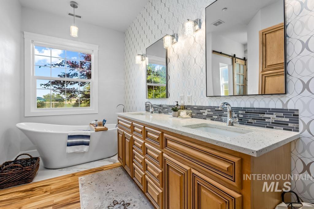 Bathroom with decorative backsplash, double vanity, a freestanding bath, and light wood-style floors