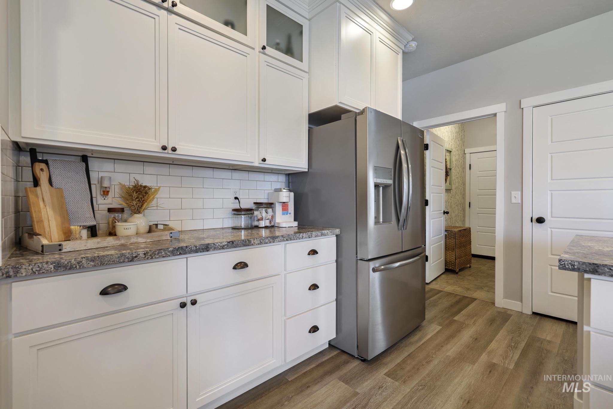 Kitchen featuring glass insert cabinets, white cabinetry, dark wood-style flooring, stainless steel fridge, and decorative backsplash