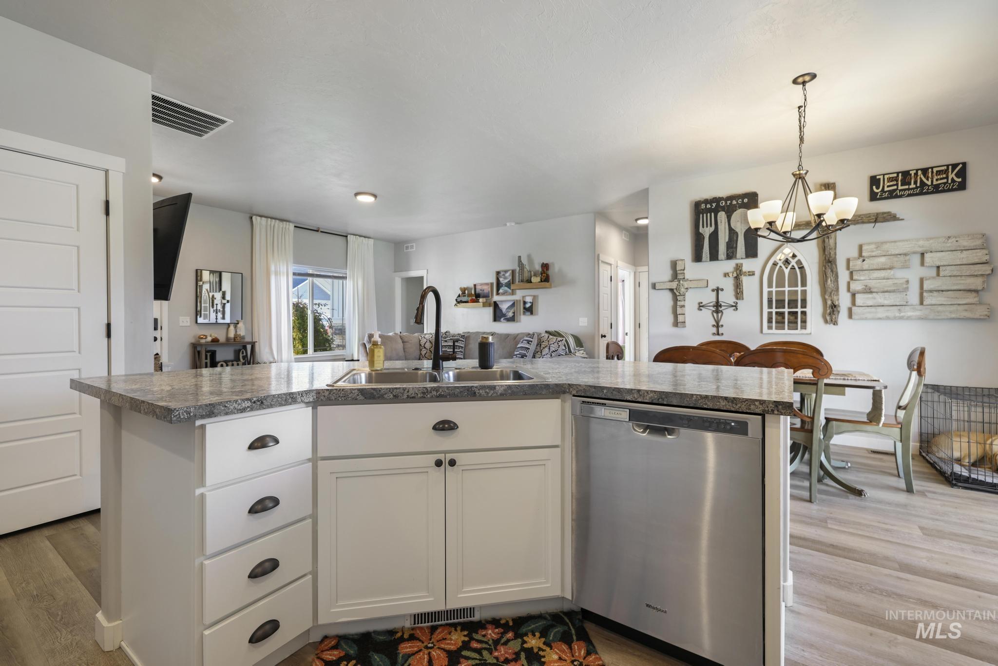 Kitchen featuring white cabinetry, a center island with sink, dishwasher, light wood-style flooring, and open floor plan