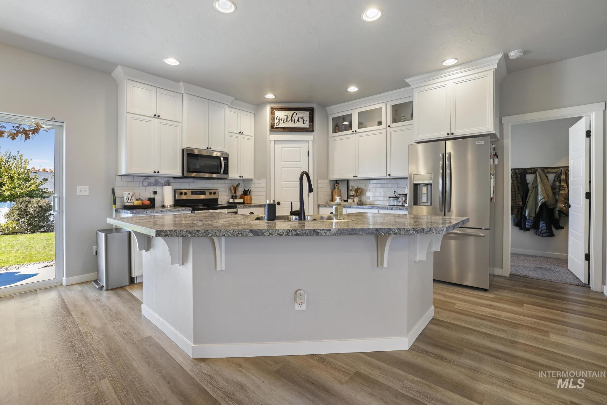 Kitchen with appliances with stainless steel finishes, white cabinetry, glass insert cabinets, recessed lighting, and a breakfast bar area