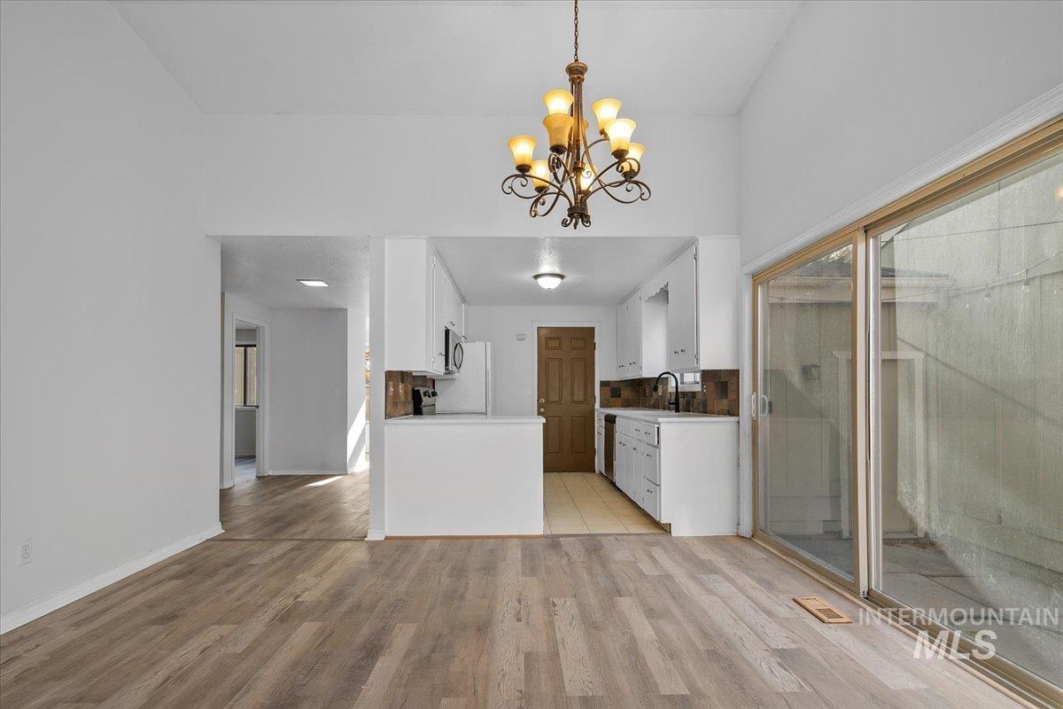 Kitchen featuring white cabinets, light wood-style floors, light countertops, pendant lighting, and a chandelier