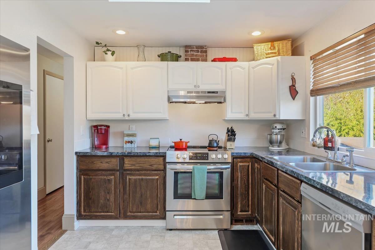 Kitchen featuring appliances with stainless steel finishes, white cabinetry, under cabinet range hood, dark brown cabinetry, and recessed lighting