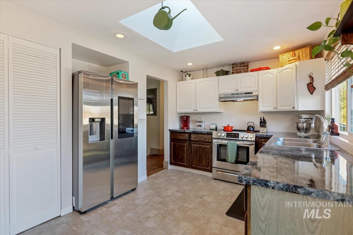 Kitchen with stainless steel appliances, white cabinetry, a skylight, recessed lighting, and dark stone counters